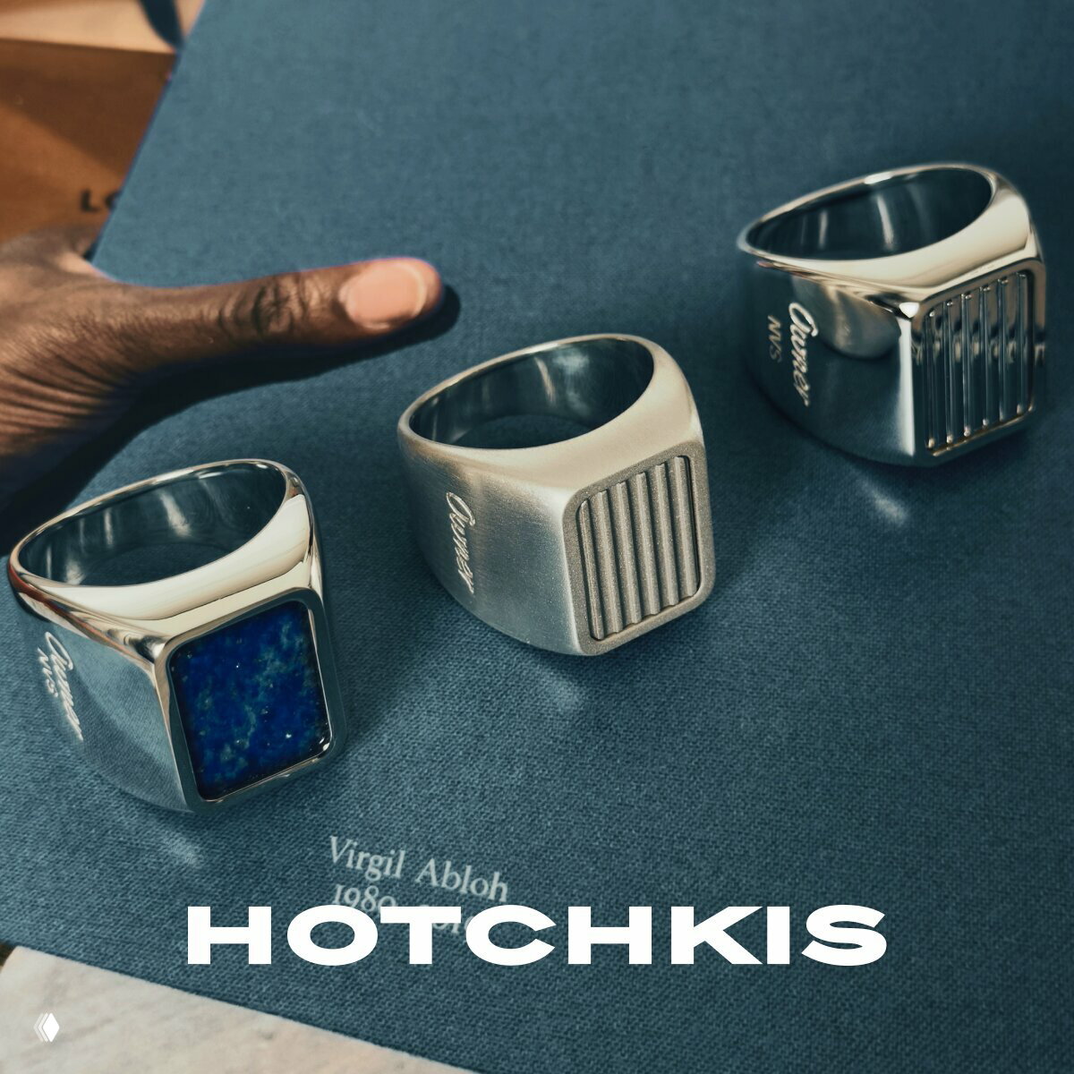 Три серебряных печатных кольца дизайнерской серии Hotchkis на синем фоне — вариации форм, текстуры и вставок в рекламной съёмке