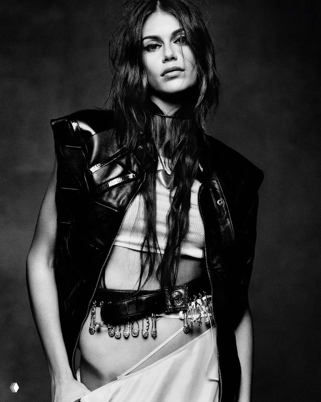 Чёрно-белый крупный портрет: модель в кожаной жилетке и поясных украшениях, акцент на глубоком взгляде и текстуре съёмки.