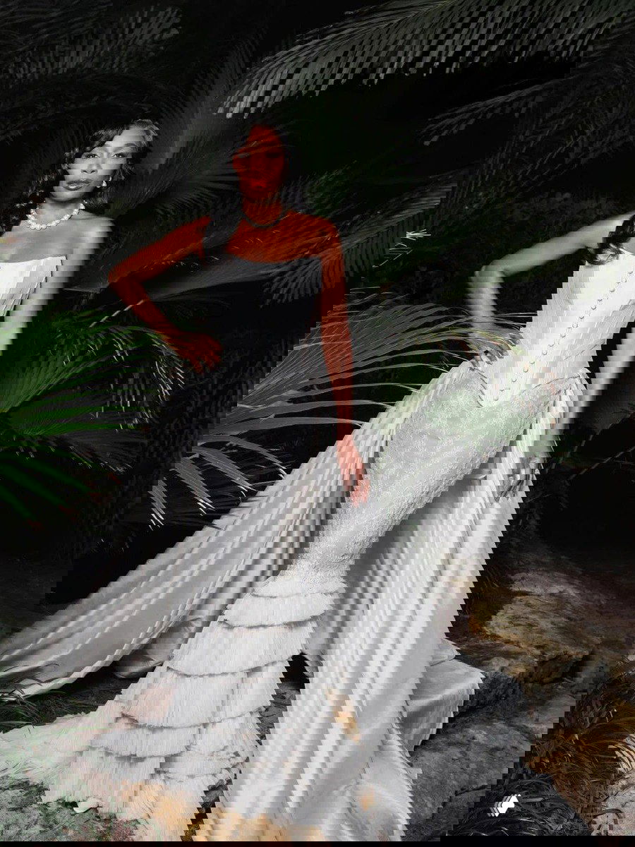 Портрет Винус в корсетном платье с многослойной юбкой и длинным шлейфом на фоне тропической зелени — богатый текстиль и драпировки в кадре.