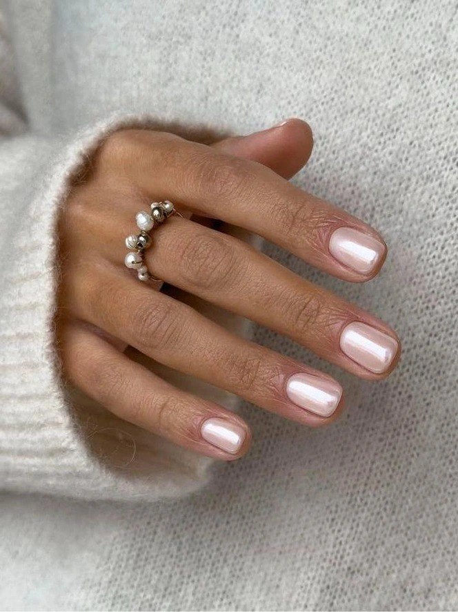 Рука в светлом свитере с аккуратными овальными ногтями в персиково-розовом перламутровом тоне и украшением-кольцом, холодная зимняя палитра.