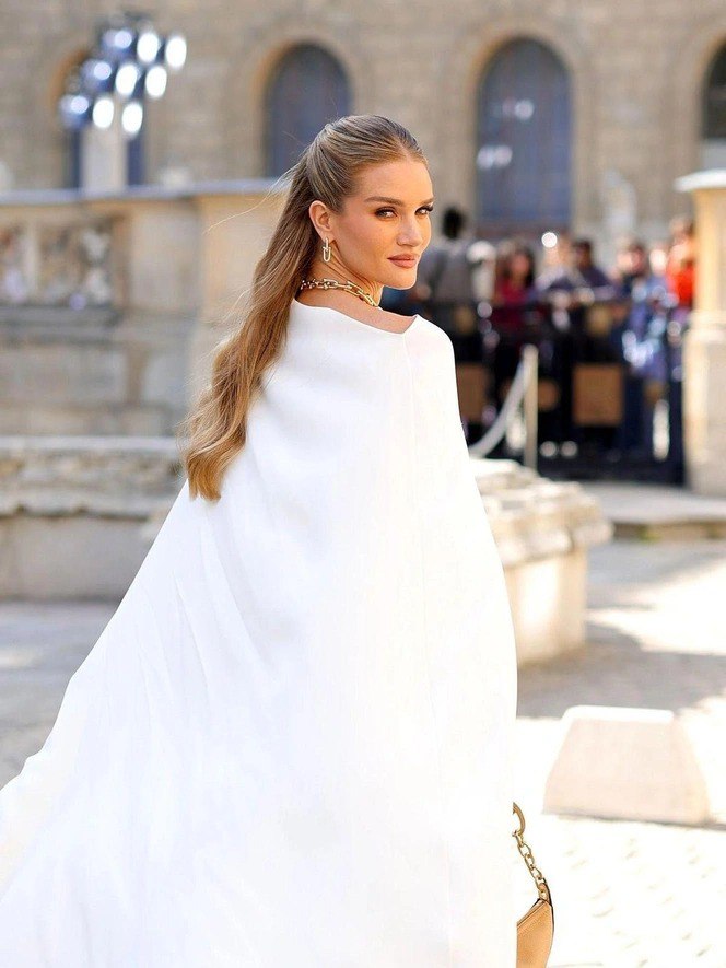 Длинные волны, собранные назад в полуоткрытую укладку; волосы уходят назад, видно плечо и силуэт на городском фоне — причёска подчёркивает верхнюю часть щёк.