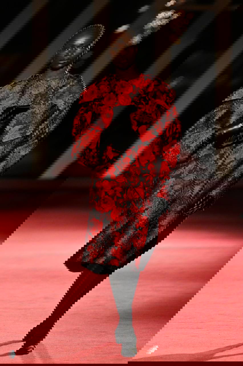 Модель в жаккардовом пальто с цветочным узором и черными перчатками демонстрирует элегантность и роскошную текстуру на подиуме Michael Kors.