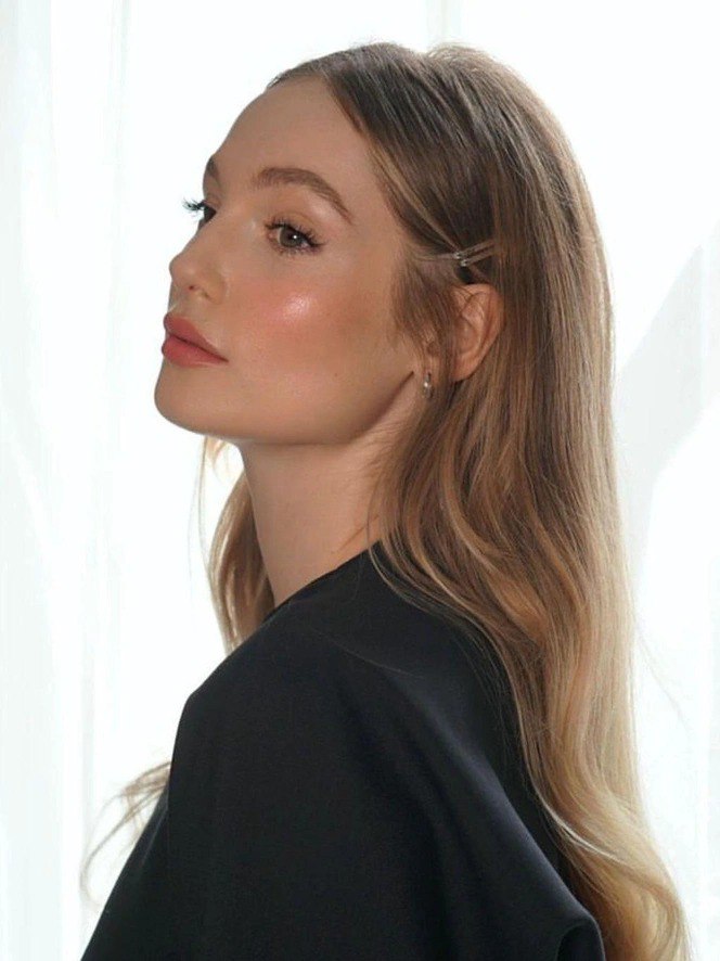 Объёмные мягкие волны с боковым пробором, волосы отведены назад и придают световые переходы на скулах; естественный дневной свет подчёркивает текстуру.