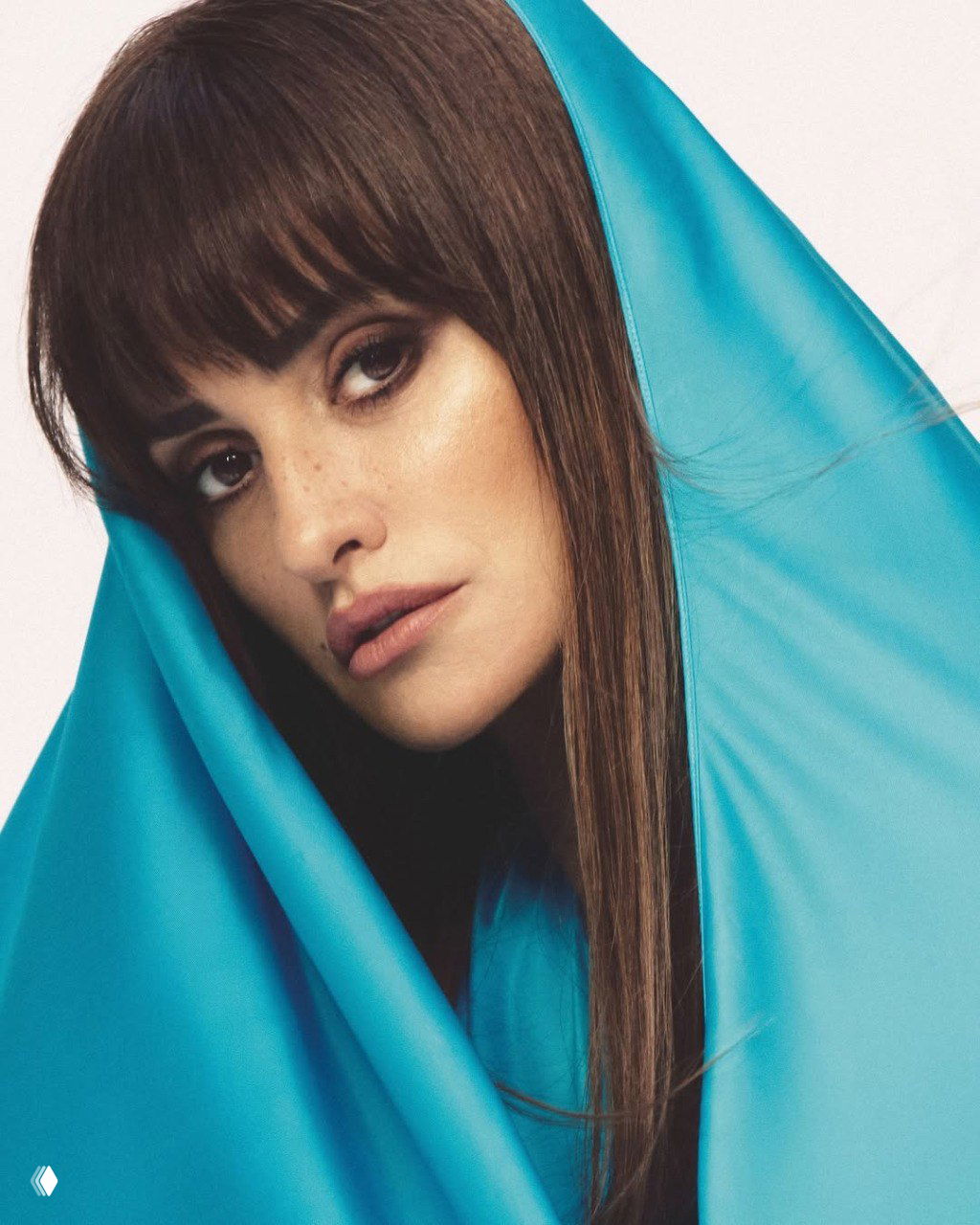 Крупный портрет женщины, частично укутанной в голубую ткань: мягкий макияж, плотная текстура ткани и спокойный задумчивый взгляд в студийной съёмке