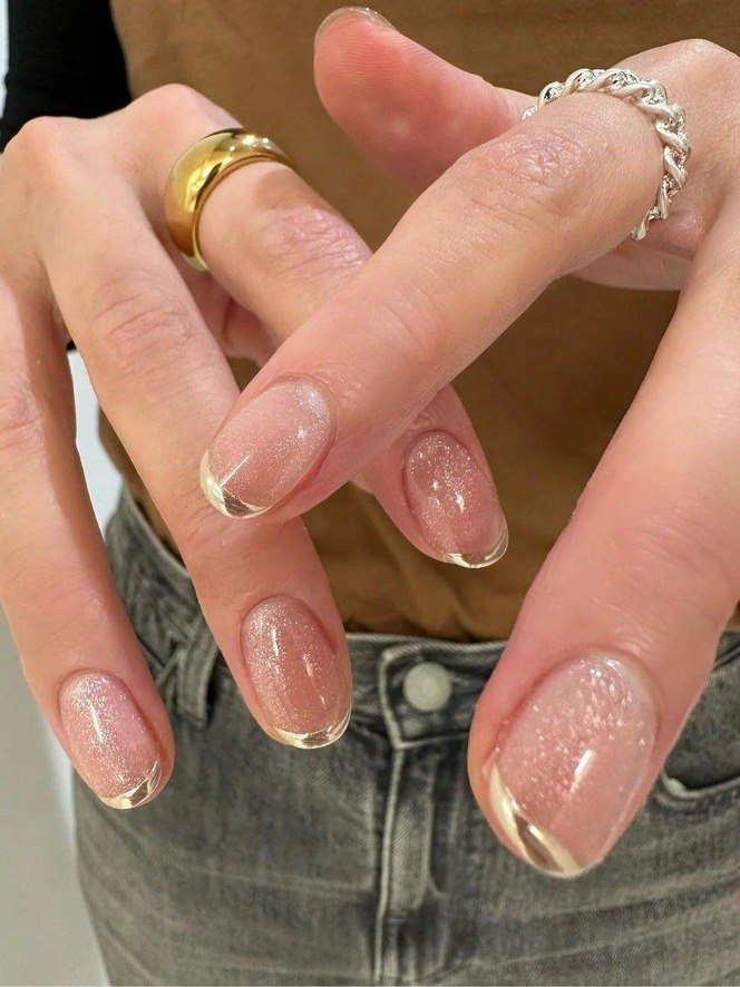 Фрагмент рук с блестящими розово-персиковыми ногтями и зеркальными золотистыми френч-акцентами — вариант для праздничного зимнего образа.