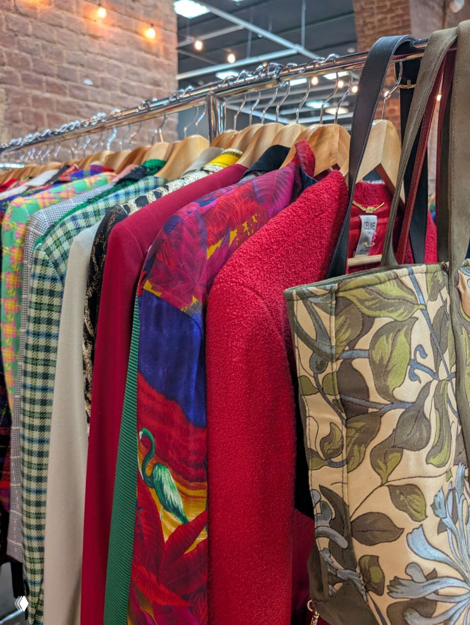 Ряд винтажной одежды на вешалке: яркие жакеты, пальто и сумки с разнообразными принтами, съемка внутри ивент-холла Мосвинтаж.