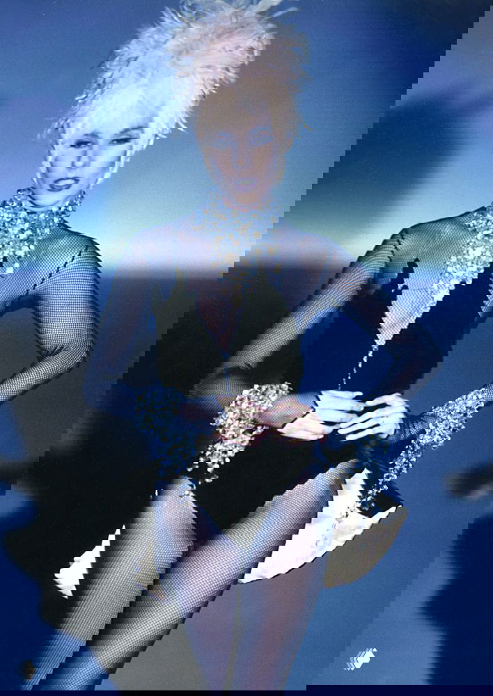 Модель в чёрном боди с сеткой и обильным украшением на шее — сценическая, элегантная деталь коллекции Mugler 1990 на подиуме.