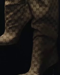 Кадр с деталями: сапоги или ткань с повторяющимся логотипом Gucci, темная студийная палитра и акцент на монограмме бренда в кампейне.
