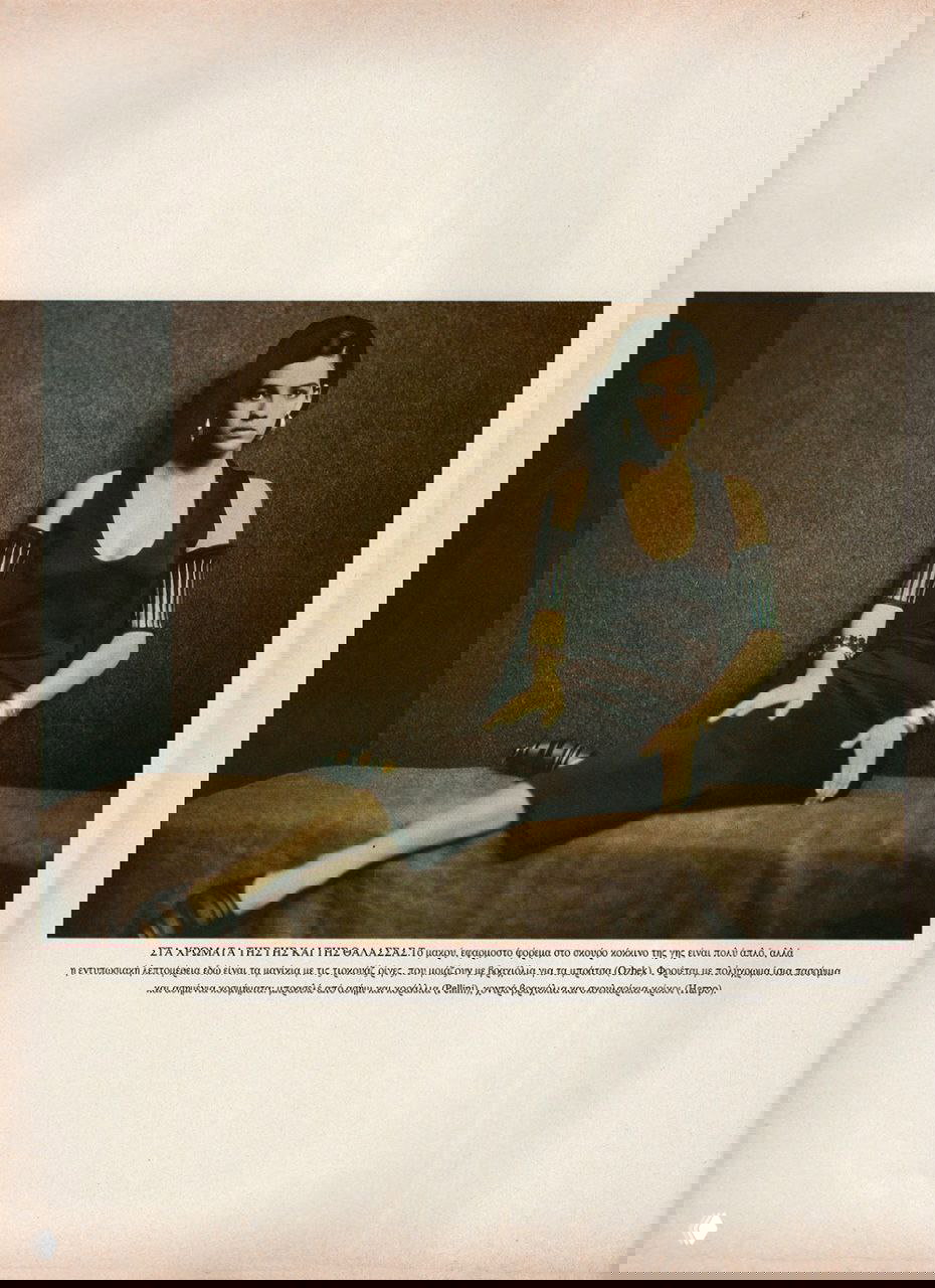 Шираз Тал сидит в тёмном платье на низкой скамье; мягкое освещение и винтажная обработка создают атмосферу архивной редакционной съемки.