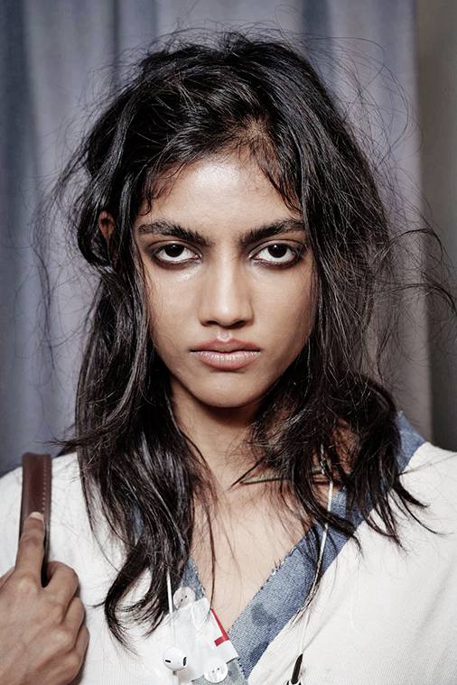 Модель с эффектом растрёпанности в волосах и более выраженным графичным взглядом: тёмные тени, подчеркнутые брови и runway‑атмосфера.