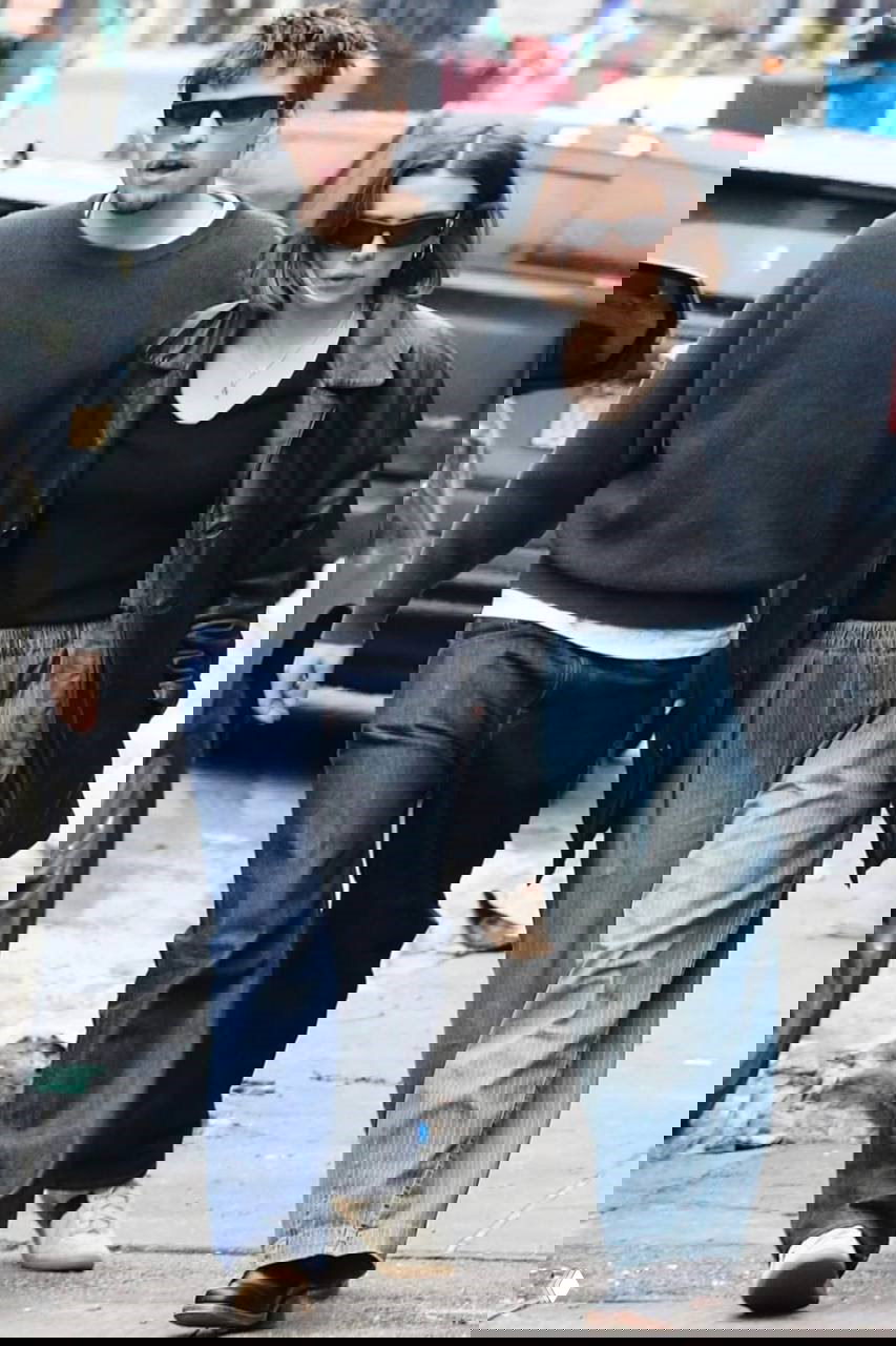 Покадровый снимок пары в повседневных образах: кожаная куртка, широкие брюки и джинсы, улица города в дневное время.