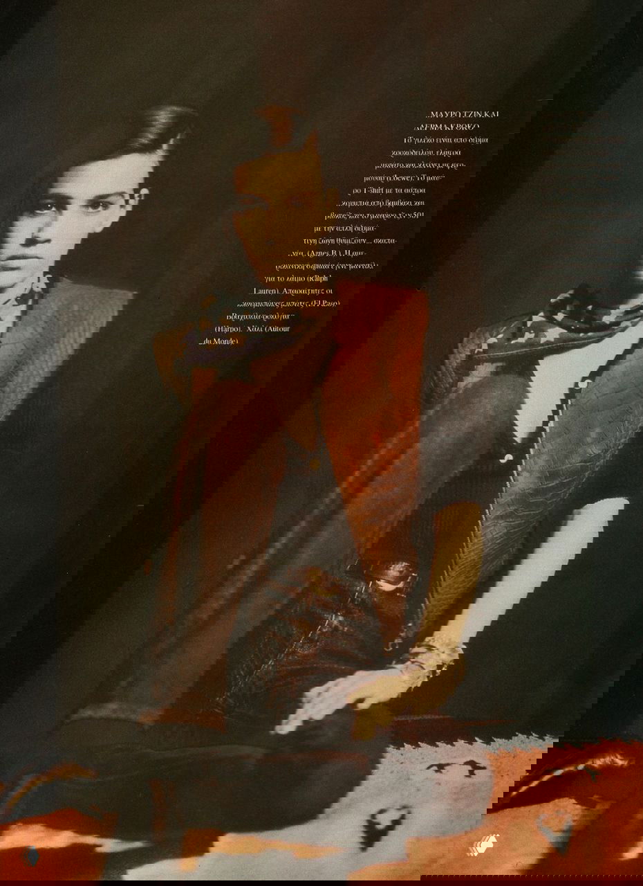 Шираз Тал в жилете и джинсах на фоне тёмной стены, поза в кресле и драматичное освещение подчёркивают модный редакционный характер снимка.