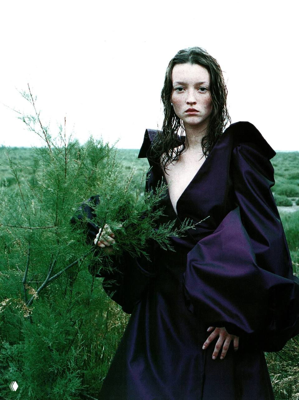 Цветная редакционная фотография: модель в насыщенно‑фиолетовом платье с объёмными рукавами стоит в зелёном поле, атмосферный кадр 1998 года.