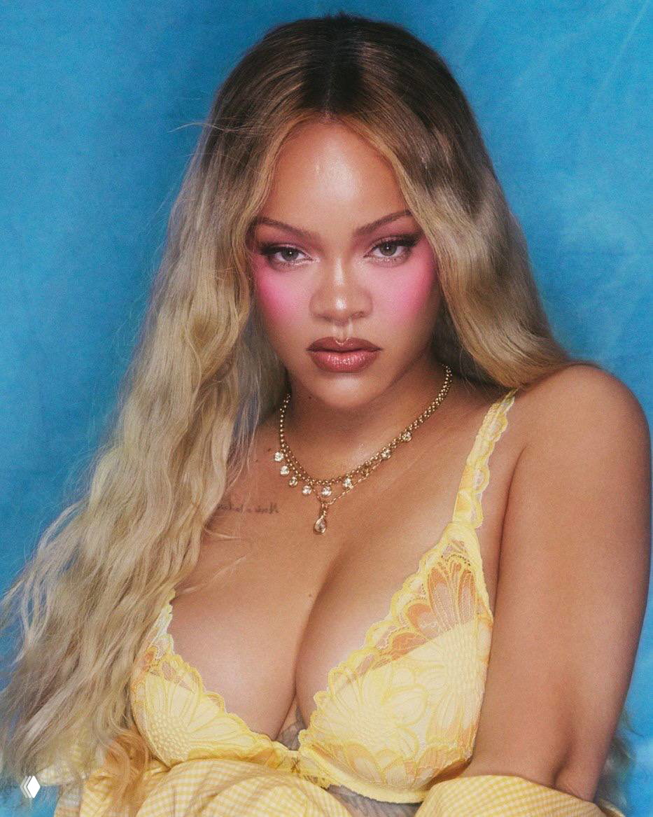 Портрет Рианны в жёлтом кружевном бра из кампании Savage X Fenty на синем фоне, крупный план с акцентом на макияж и декольте