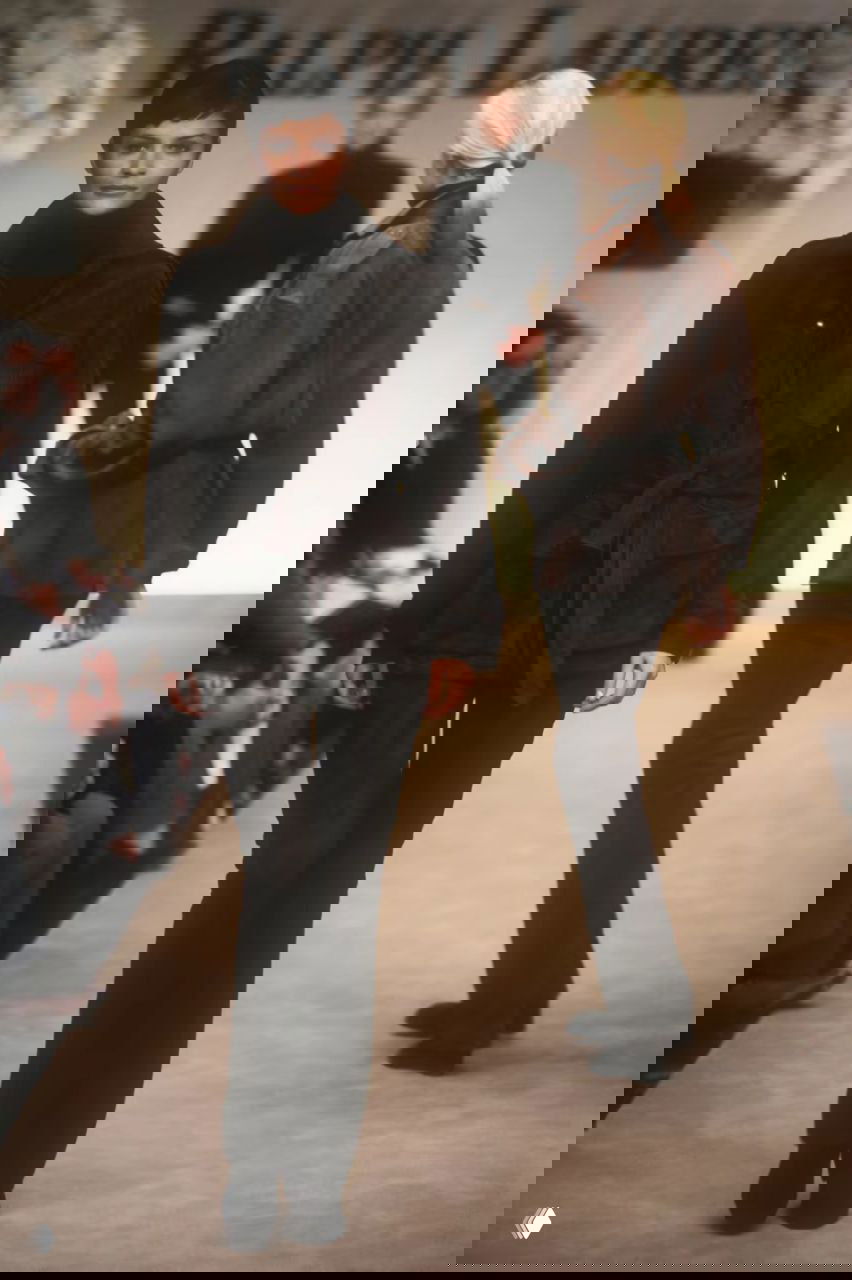 Модель в темно-коричневом костюме и поясной куртке шагает по шоу Ralph Lauren; минимализм и утончённая простота 1996 года.