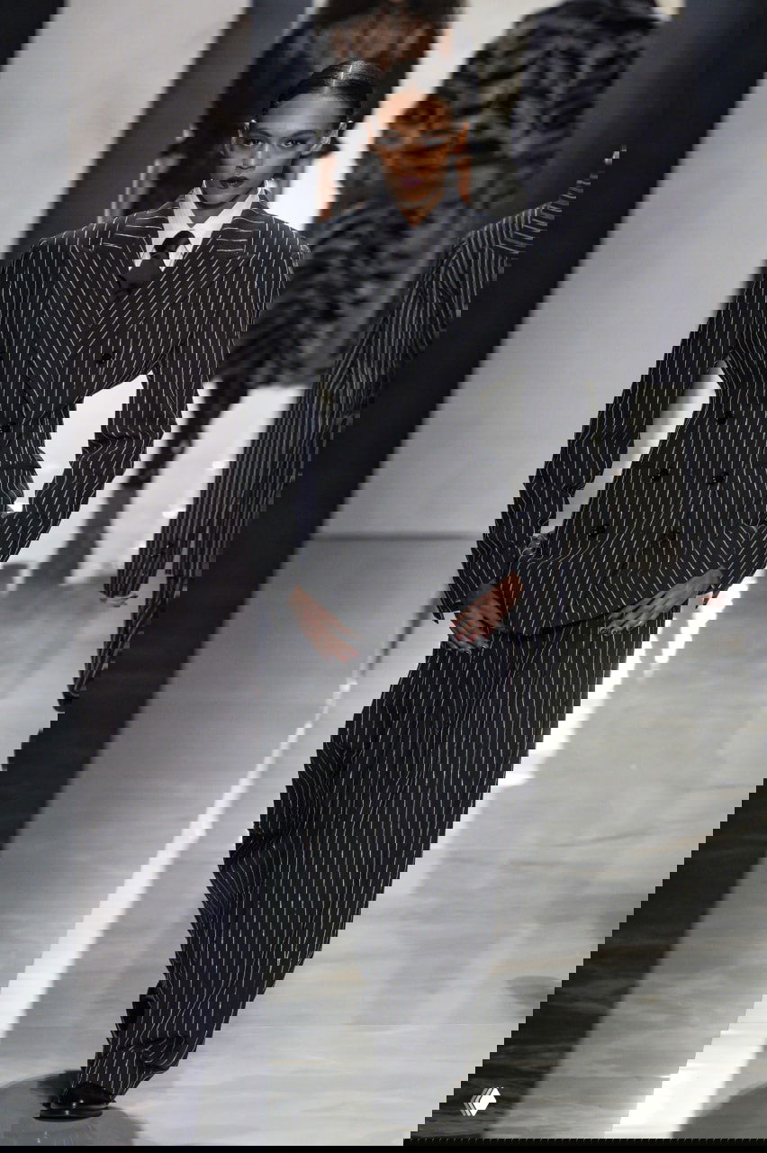 Женский образ в двубортном полосатом костюме с галстуком, подчёркнутые плечи и строгость силуэта на показе D&G осень‑зима 2026/27.