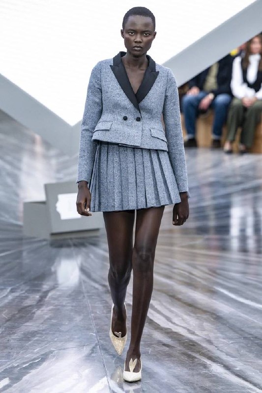Модель в сером пиджаке с укороченным кроем и плиссированной мини-юбкой, демонстрирующая адаптацию низкой талии в классическом силуэте.