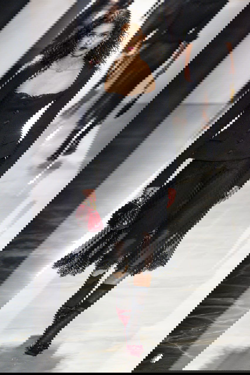 Модель в приталенном жакете и прозрачной кружевной юбке, тёмная палитра и текстуры — кадр с показа Dolce & Gabbana FW 2026/27.