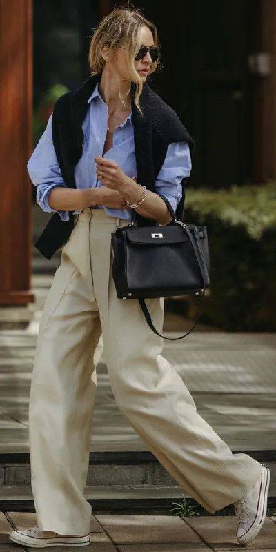 Динамичный кадр: широкие бежевые брюки в уличном движении, рубашка голубого тона и чёрная сумка — пример работы силуэта в жизни.