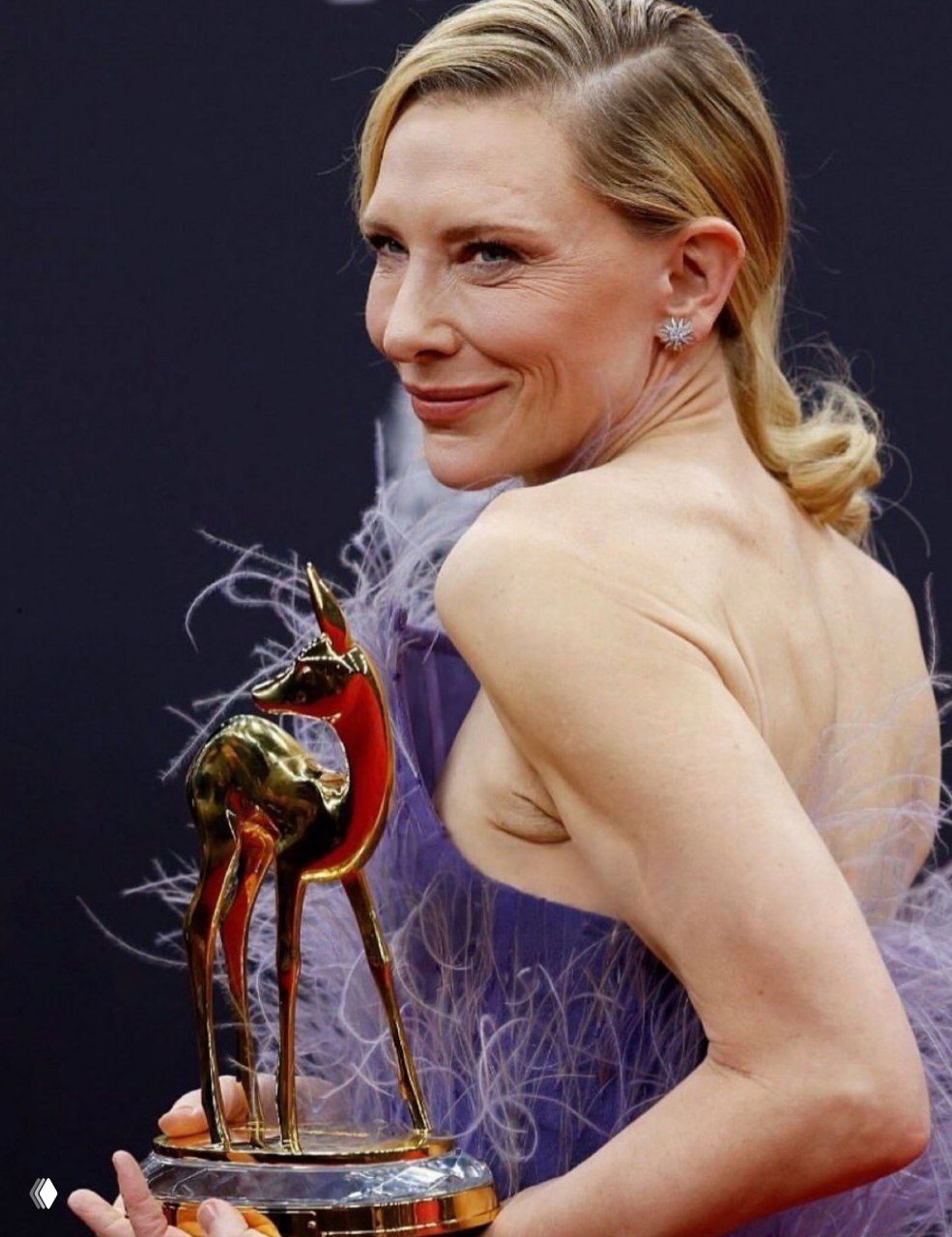 Крупный план Кейт Бланшетт со статуэткой Bambi; видна фактура фиолетовых растительных перьев на платье Stella McCartney.