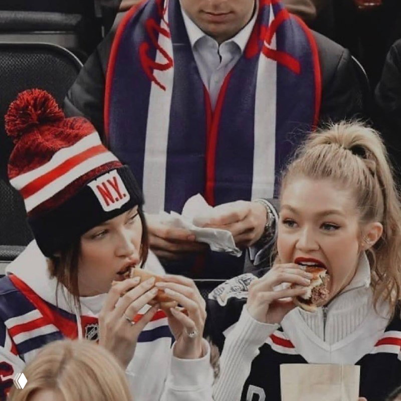 Кадр на спортивном мероприятии: две женщины в теплой одежде едят бургеры, динамичный снимок в категории «повседневный стиль» и уличная эстетика.