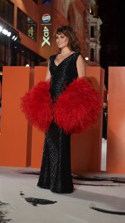 Актриса на красной ковровой дорожке в чёрном длинном платье и с объёмной ярко-красной перьевой накидкой, полный рост.