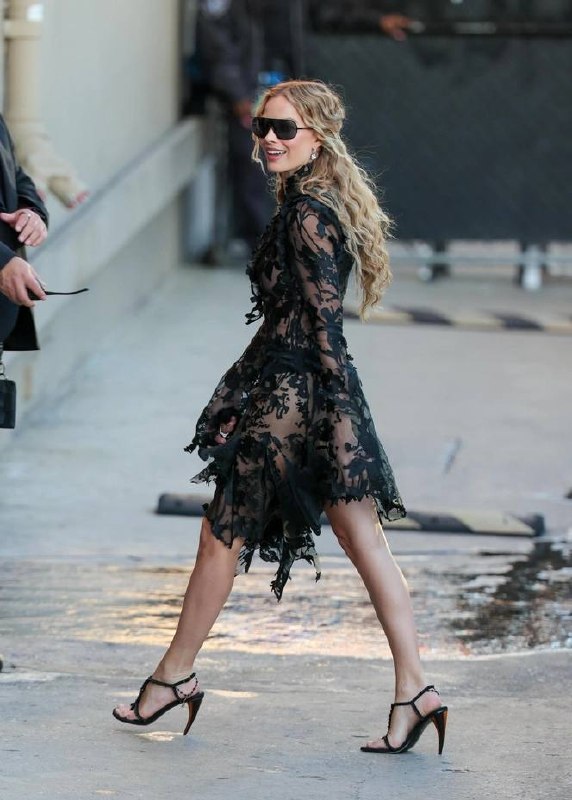 Женщина в черном кружевном платье с рваными краями и полупрозрачными вставками на городской улице; образ с драматичной, литературной эстетикой.