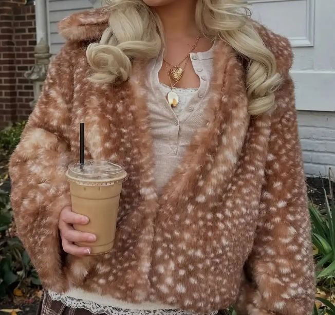 Рука с кофе и коричневая шуба с нежным пятнистым 'Бэмби'‑рисунком; деталь уличного аутфита в тёплой цветовой гамме для повседневного образа.