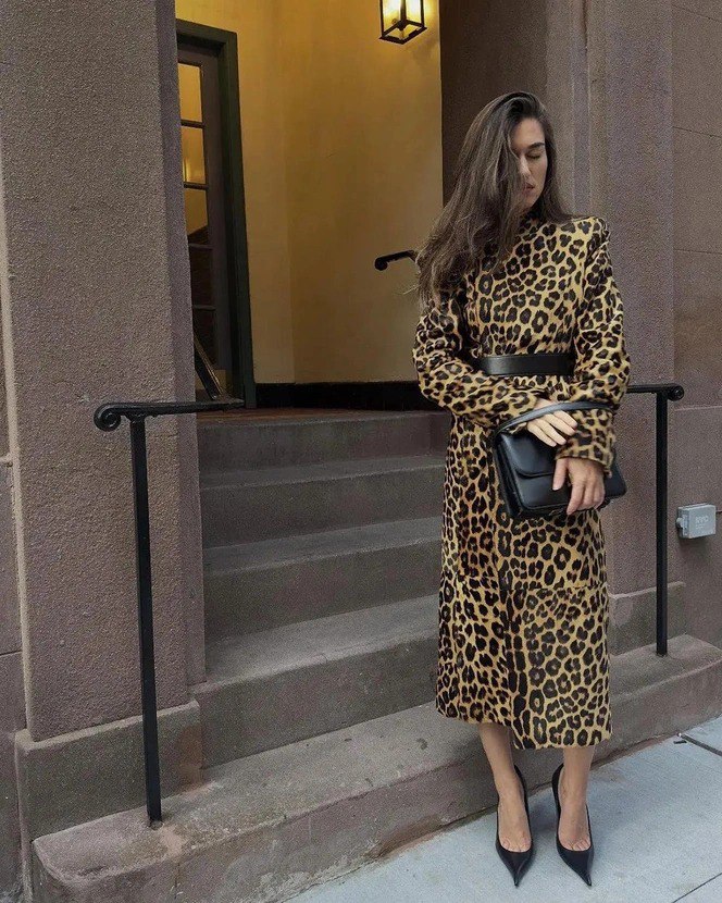 Стильный кадр у ступеней: женщина в длинном пальто с леопардовым принтом, с поясом и кожаной сумкой позирует у входа городского дома.