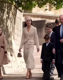 Женщина в кремовом костюме ведёт группу людей и детей по улице у стен Виндзорского замка в день пасхального мероприятия.