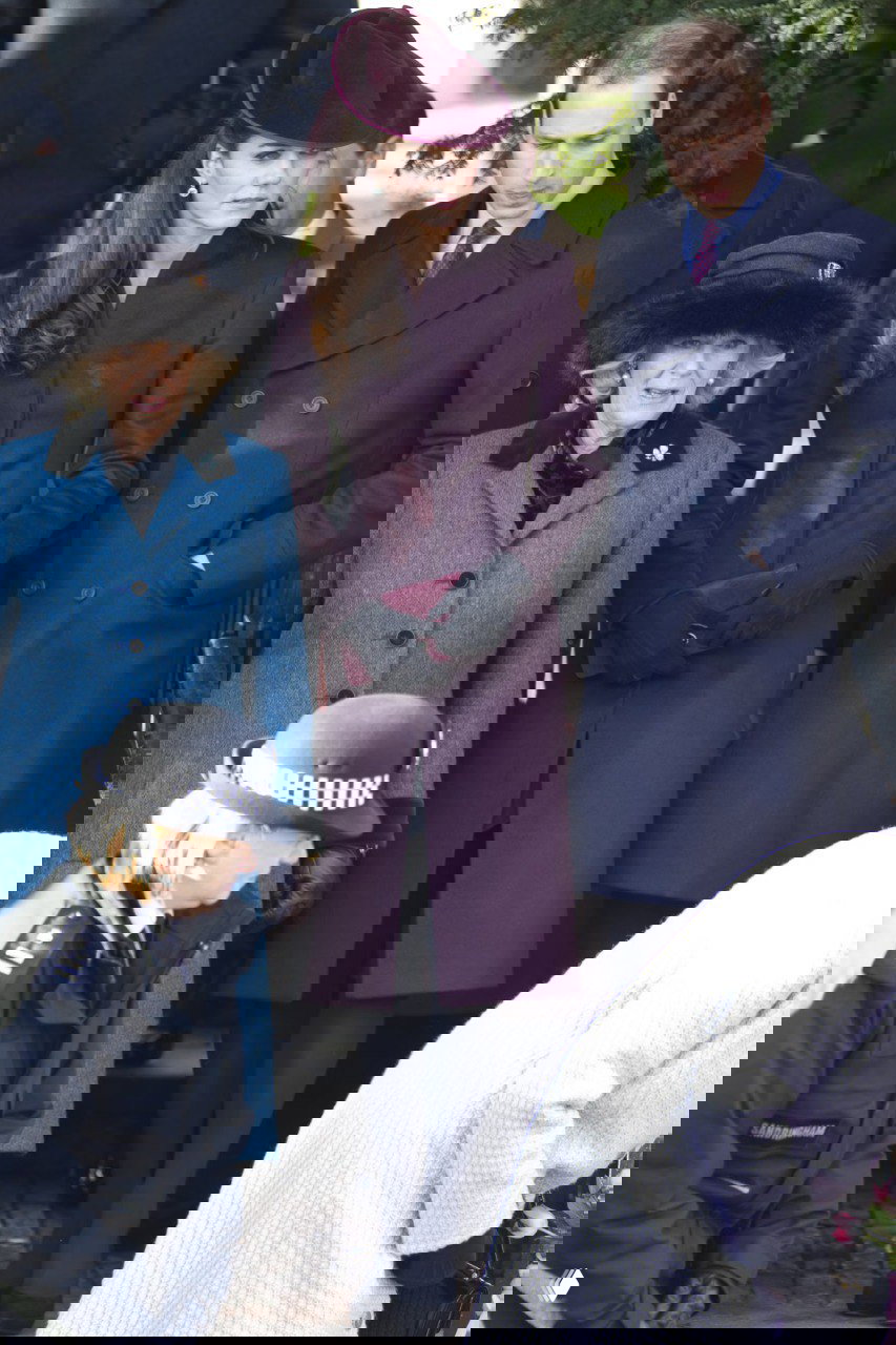 Трое взрослых в зимних пальто и шляпах стоят у входа, окружающие люди и полиция в кадре подчёркивают публичный характер торжественного события.