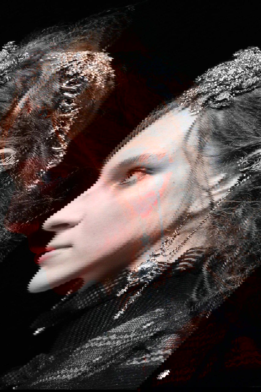 Крупный план головы модели с декоративным ободком и массивными висячими серьгами, демонстрирующий акцентные аксессуары и детализацию.