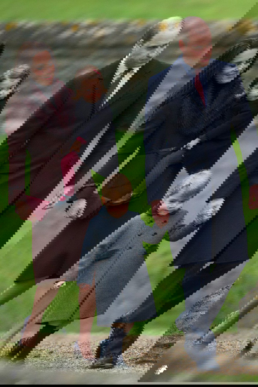 Семейный кадр: двое взрослых и двое детей в тёплой одежде идут по газону — классические пальто и детские пальто создают праздничную картину.