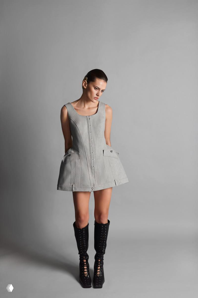 Студийный портрет: модель в сером корсетном платье с расширенной баской и накладными карманами, образ завершён высокими шнурованными ботфортами.