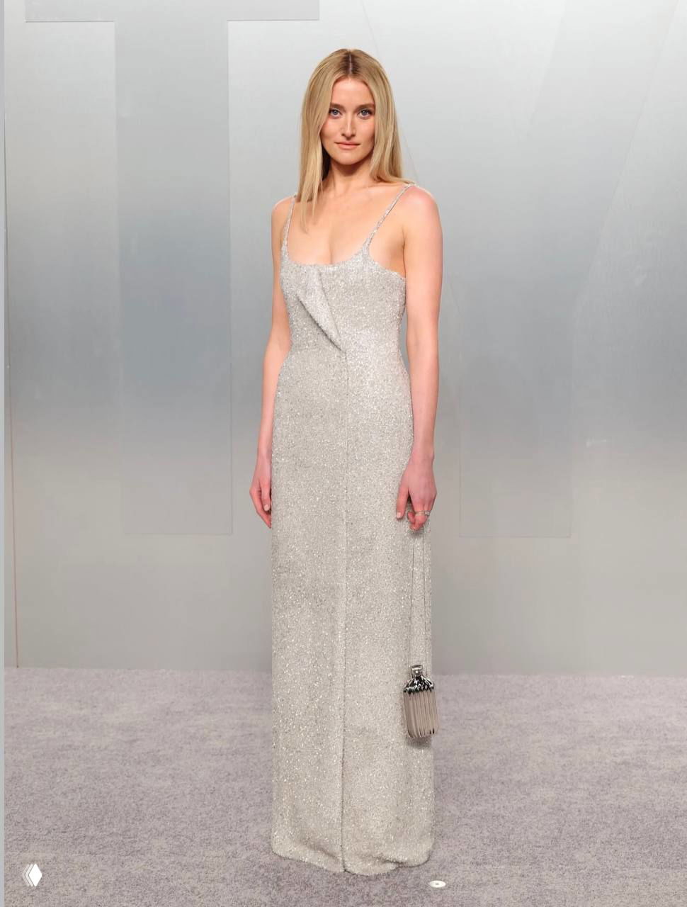 Женщина в тонком серебристом платье‑комбинации на бретелях с маленькой сумочкой, минималистичный образ на ковре афтепати Vanity Fair.