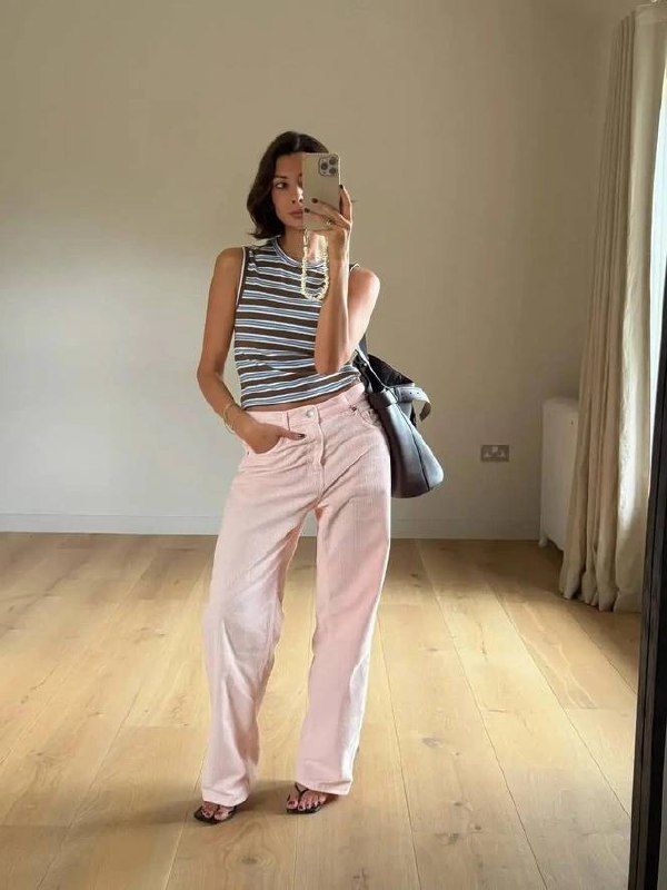 Инстамиррор: девушка в светло‑розовых джинсах и полосатом топе делает селфи в светлой комнате на фоне паркета.