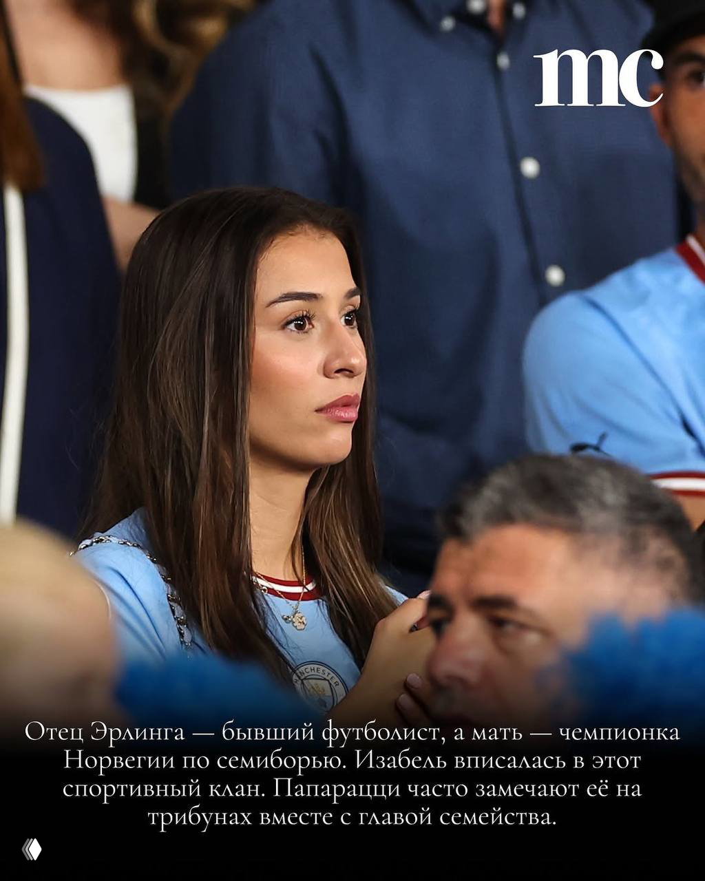 Крупный план женщины на трибуне в светло‑голубой футболке; серьезный взгляд, окружающие болельщики на фоне.