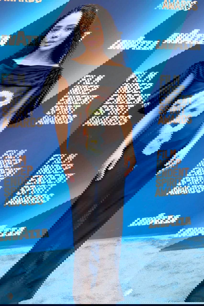 Гостья в прозрачном чёрном платье с цветочным мотивом по центру на синем фоне фотозоны; виден полный рост и укладка волос.