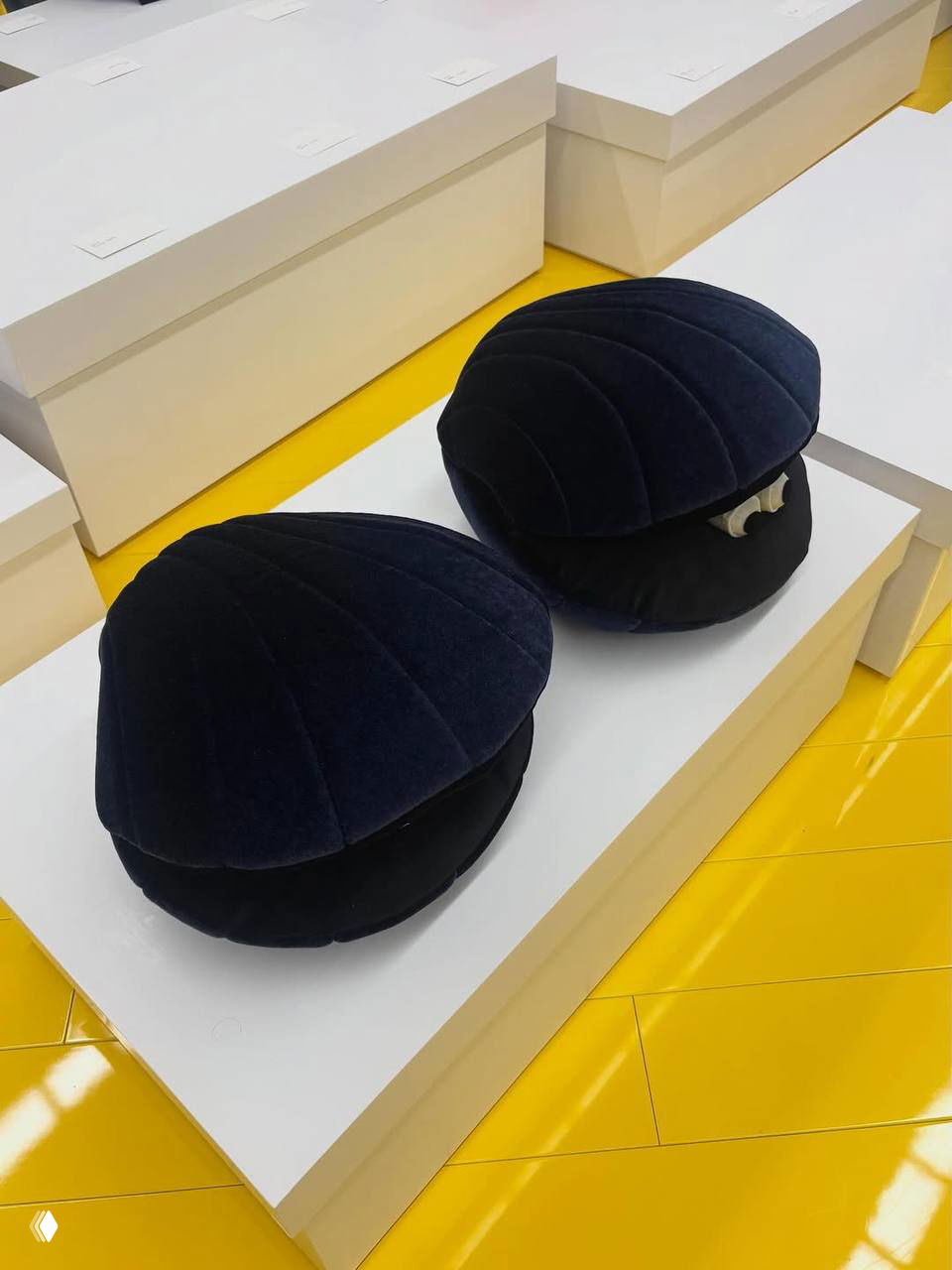 Пара плюшевых раковин на белой платформе на фоне зала и жёлтого пола — деталь инсталляции на показе Loewe (фото Vogue)