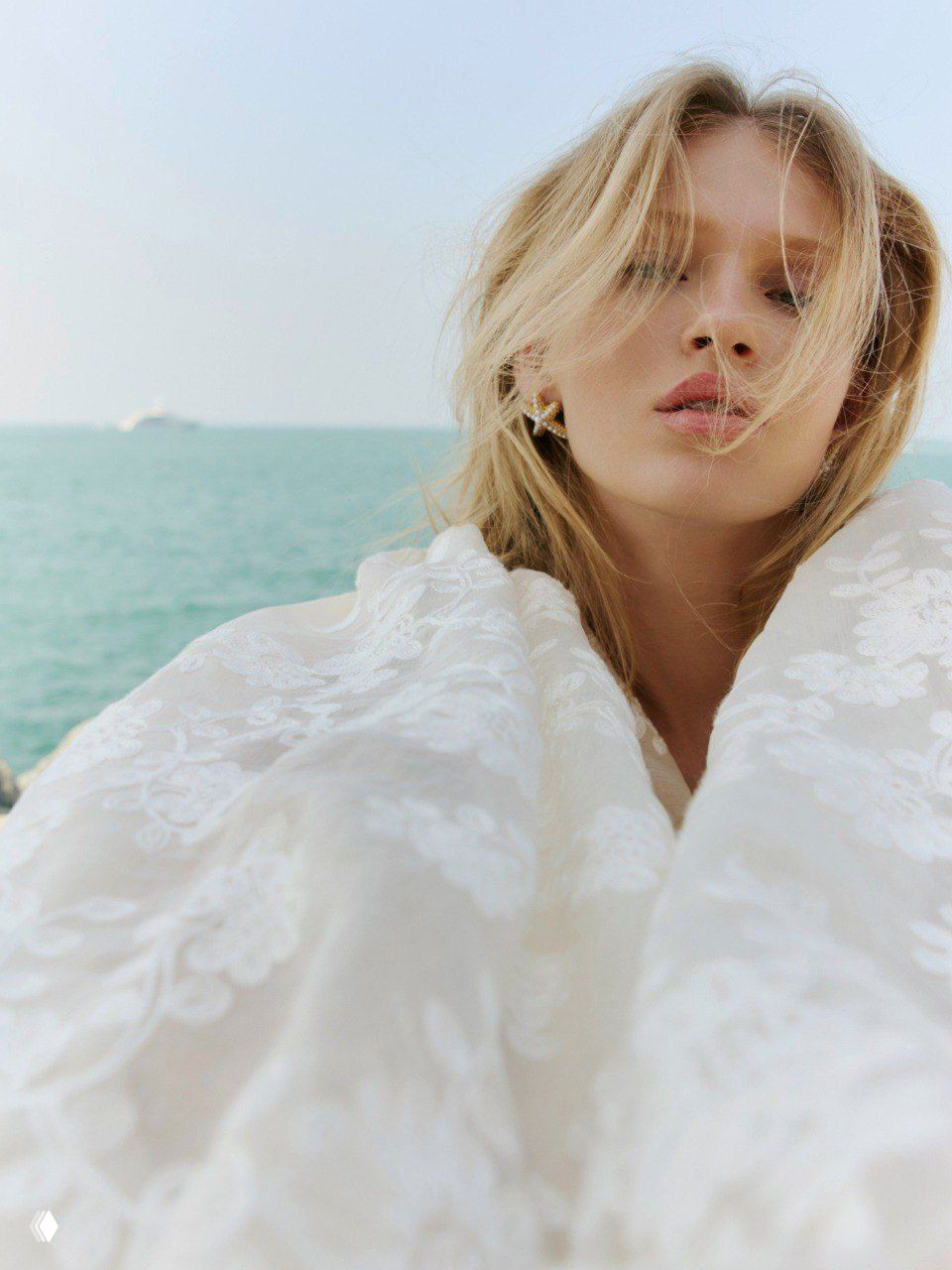 Портрет модели на морском фоне в легком белом халате или плаще с тонкой фактурой — морская эстетика и естественный макияж в фокусе.