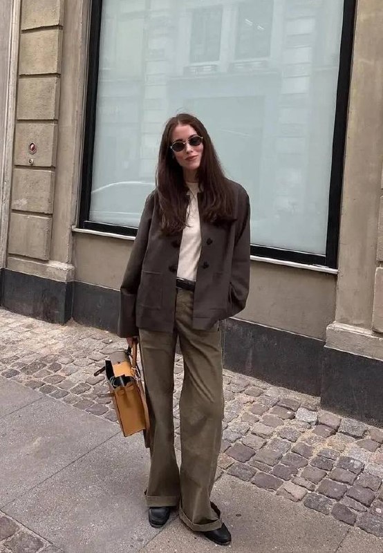 Городской стритстайл: модель в оливковых (хаки) широких джинсах, тёмном жакете и кожаных туфлях идёт по булыжной мостовой.