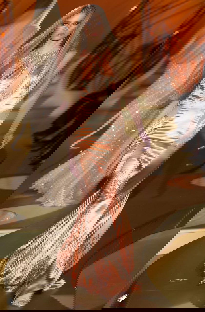 Модель в персиковом атласном длинном платье Versace 2004 с мерцающими вставками и облегающим силуэтом на фоне ступенчатого подиума и золотого оформления сцены.