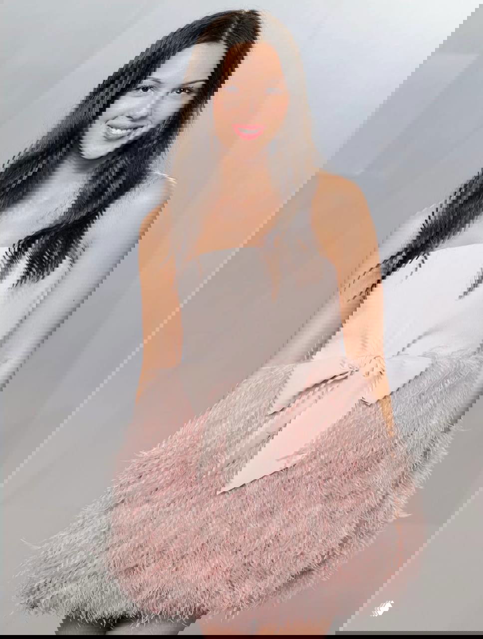 Женщина в пастельном розовом платье с пышной перьевой юбкой и крупным бантом на поясе, романтический образ на вечеринке Vanity Fair.