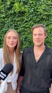 Двое гостей на фоне плотной зелёной лианы на мероприятии Marie Claire: женщина и мужчина в элегантной одежде у микрофона.