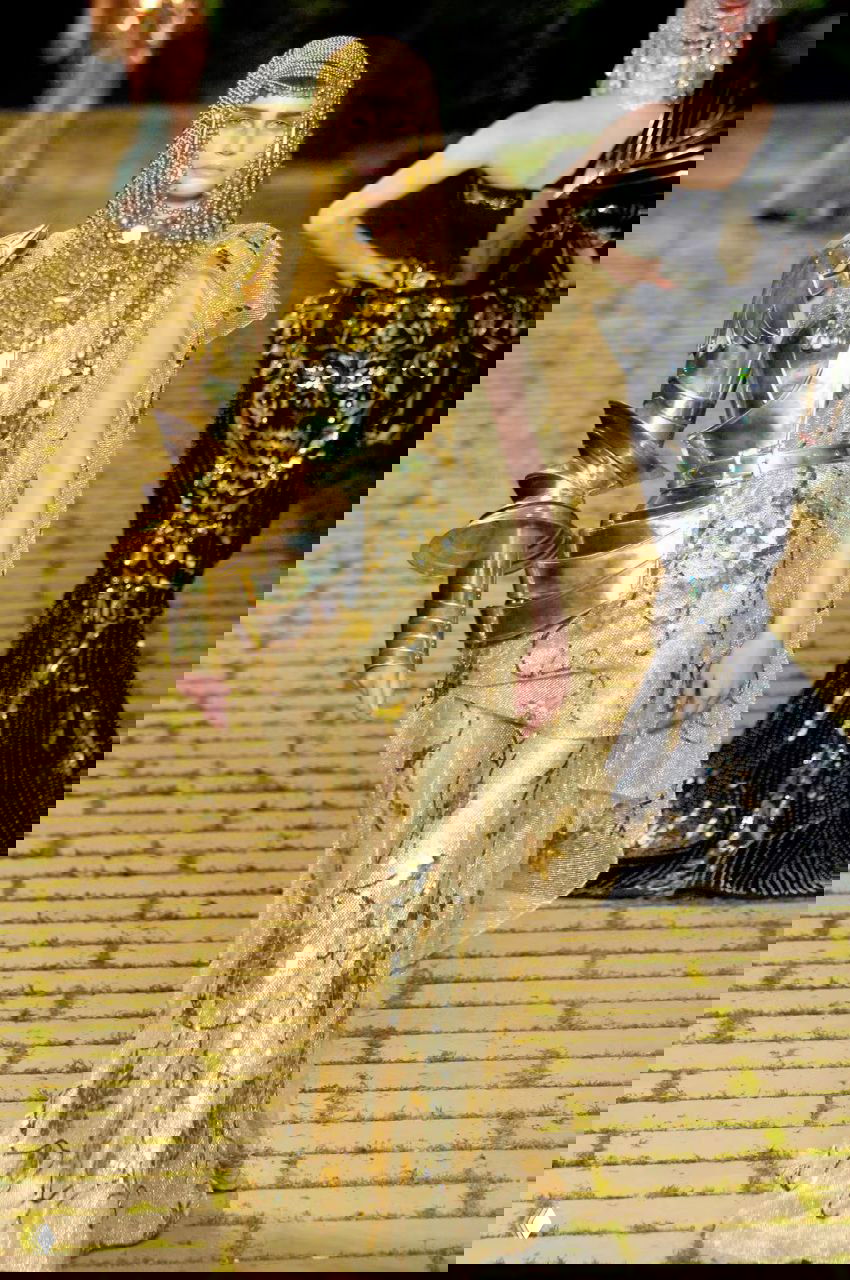 Золотой кутюрный наряд Dior 2006: модель в сверкающем платье и массивной золотой броневой конструкции на плече, образ в стиле принцессы-воительницы.