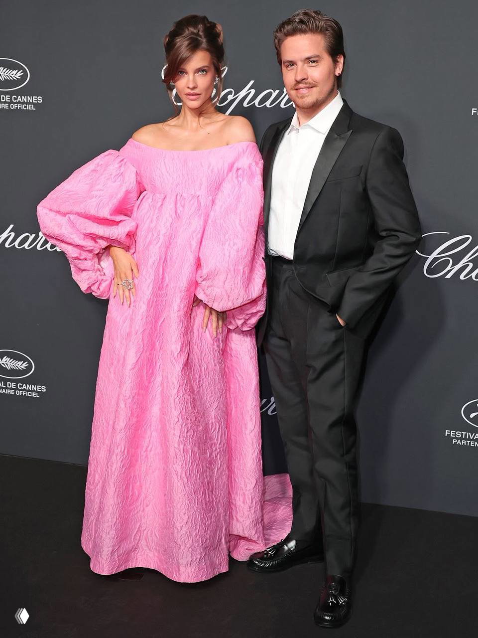 Пара позирует у чёрной фотозоны Chopard: Барбара в розовом наряде, Дилан Спроус в смокинге — классический светский кадр с мероприятия в Каннах.