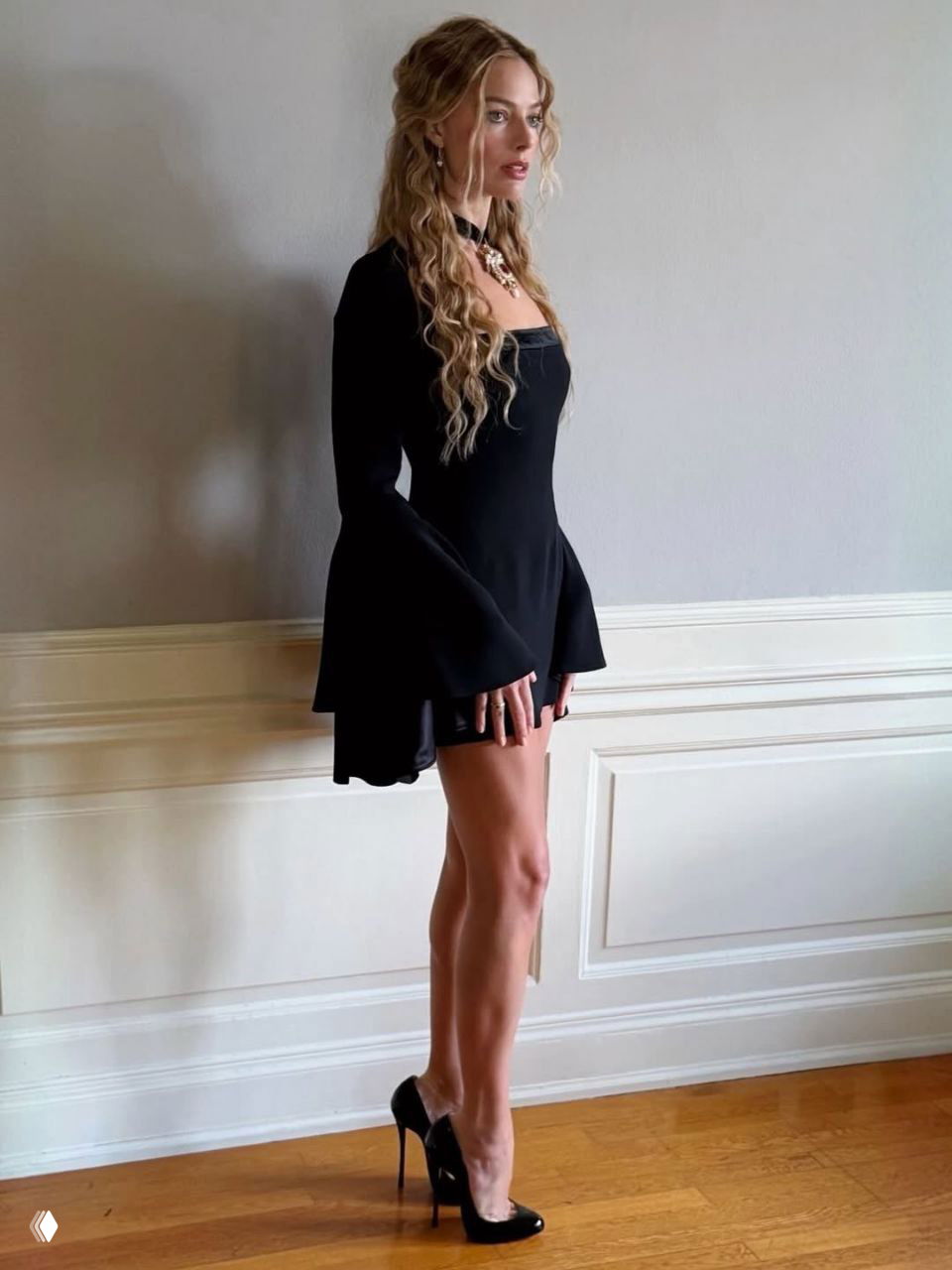 Профильный кадр Марго Робби в обтягивающем чёрном платье с расклешёнными рукавами и лаковыми туфлями — полный рост, интерьерный фон.