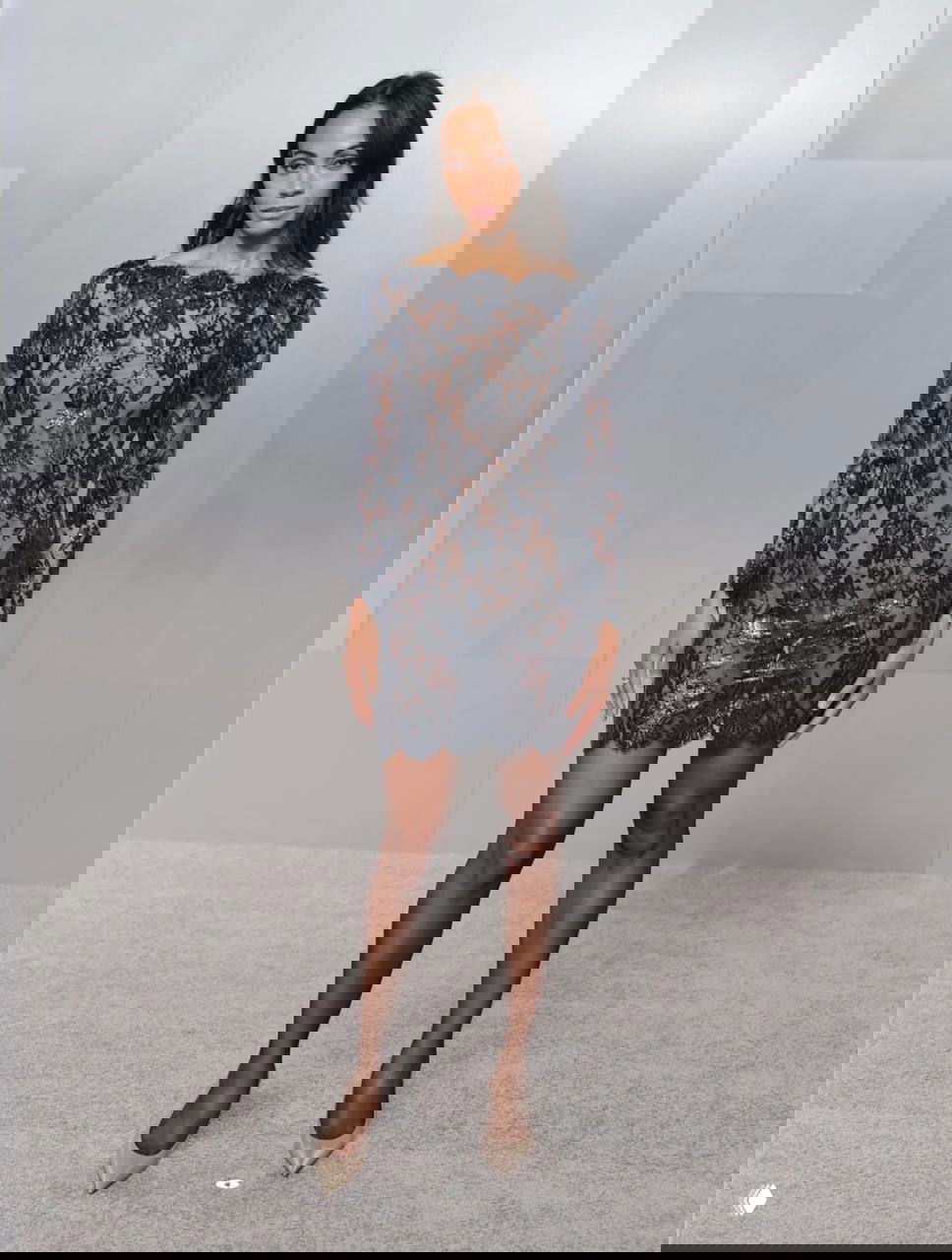 Женщина в тёмном кружевном мини‑платье с прозрачными вставками и блёстками, классическая туфельная пара и элегантная поза на фотозоне.