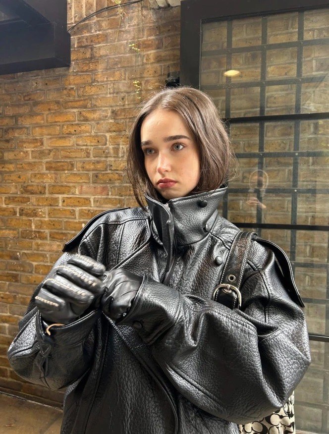 Модель в большом чёрном кожаном пальто с высоким воротником, пряди волос заправлены внутрь, акцент на фактуре верхней одежды
