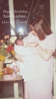 Цветное детское фото: Жаклин Адамс держит новорожденную Викторию в белом платье среди цветов и поздравительной надписи на снимке.